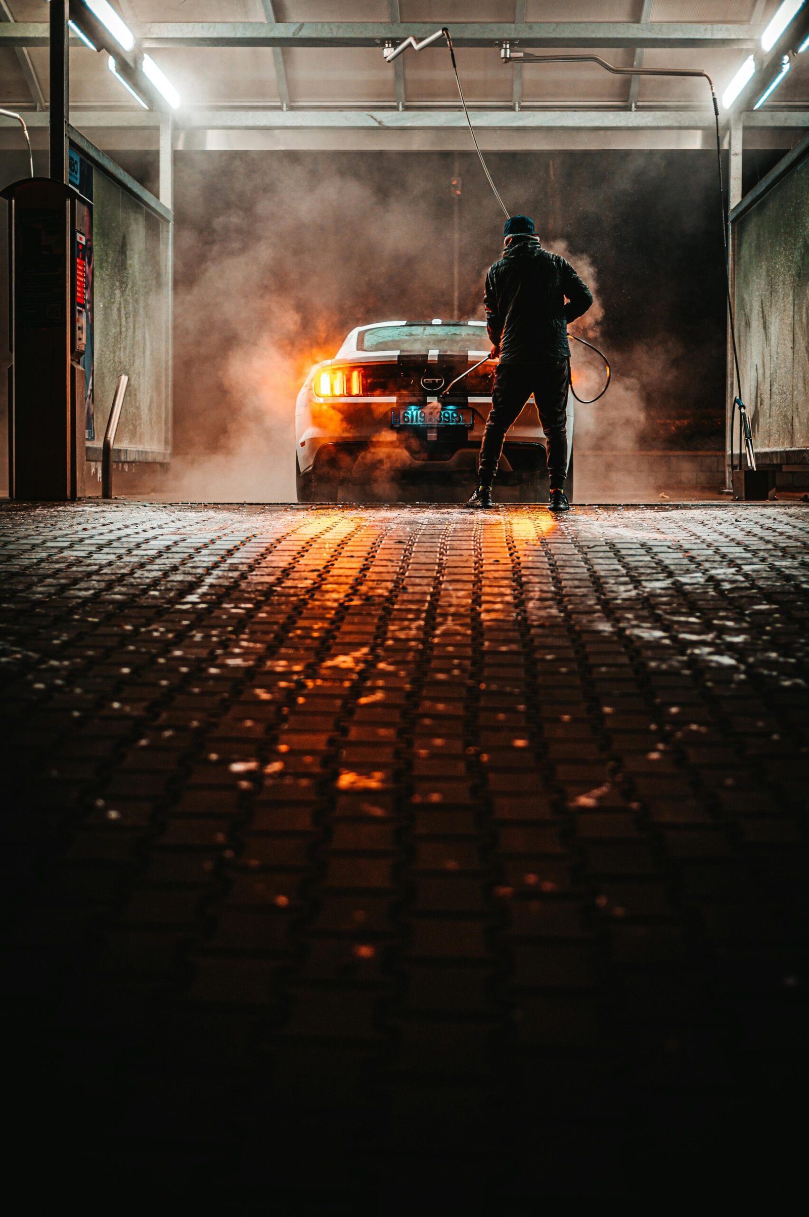 A person washing a sports car at a carwash during the night, illuminated by lights.